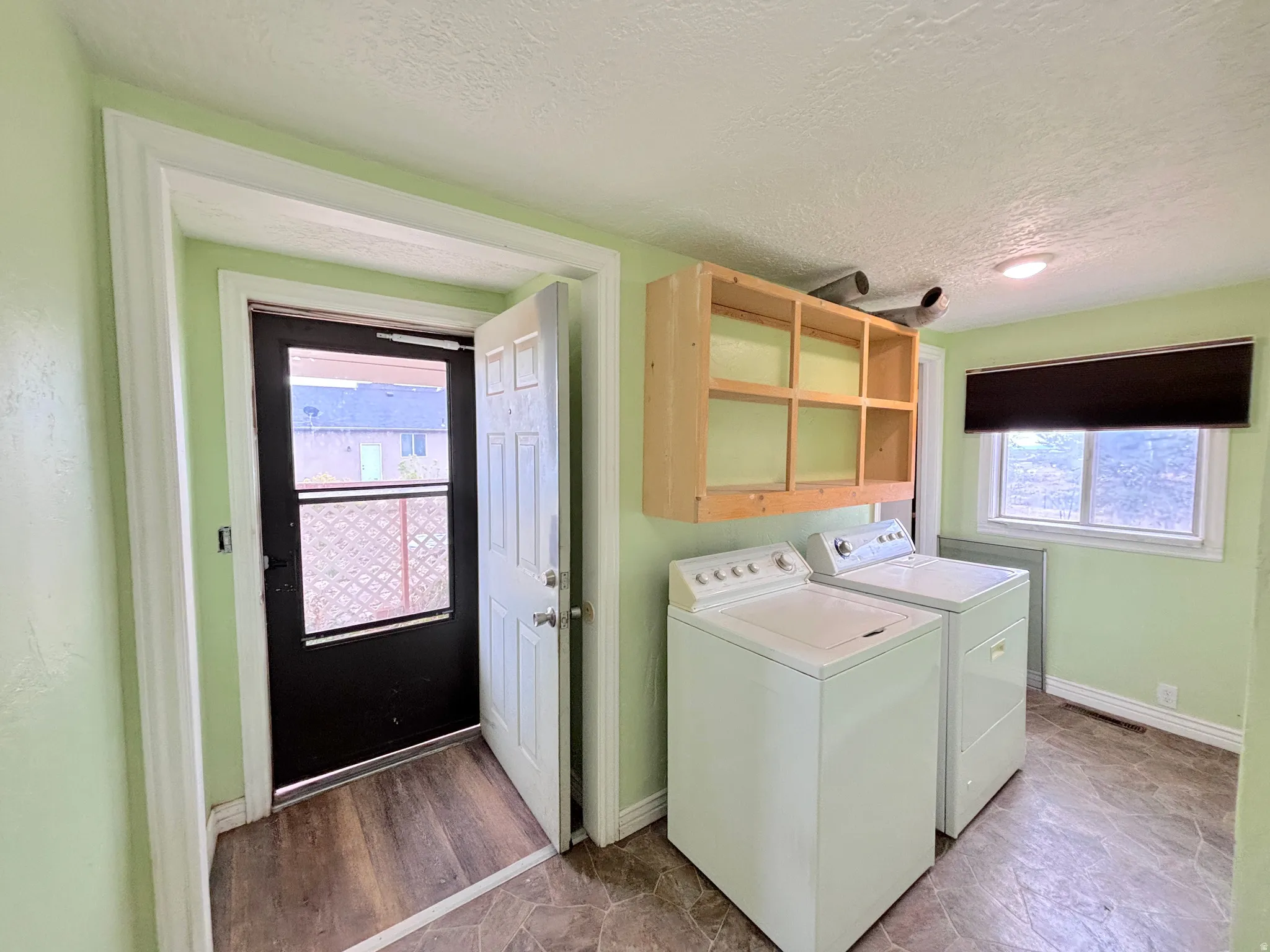 Dedicated laundry area with wood-finish flooring, natural light through a window, and a wall-mounted shelving unit