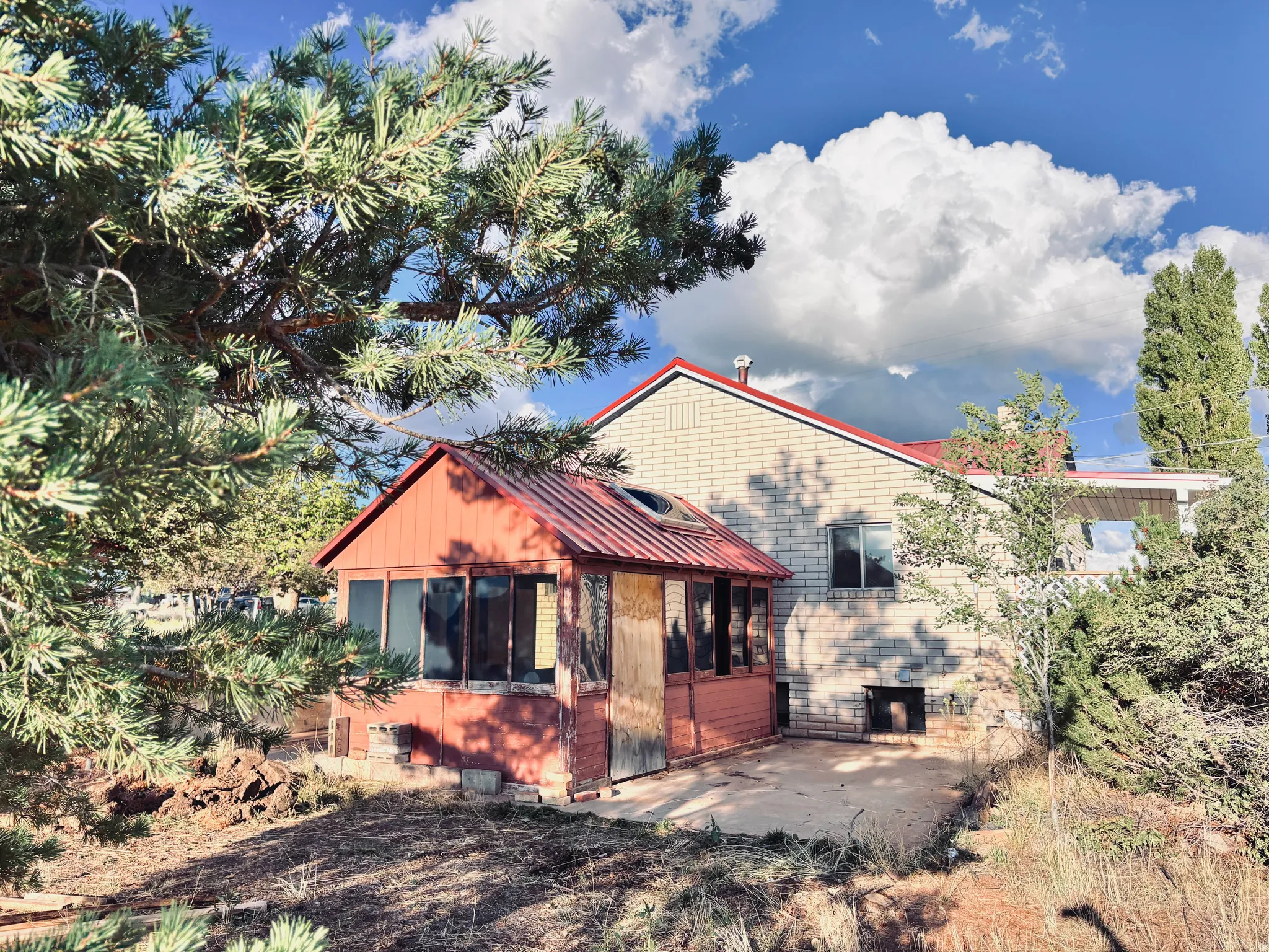 Brick exterior with a red metal roof and an enclosed porch featuring multiple windows and a round skylight