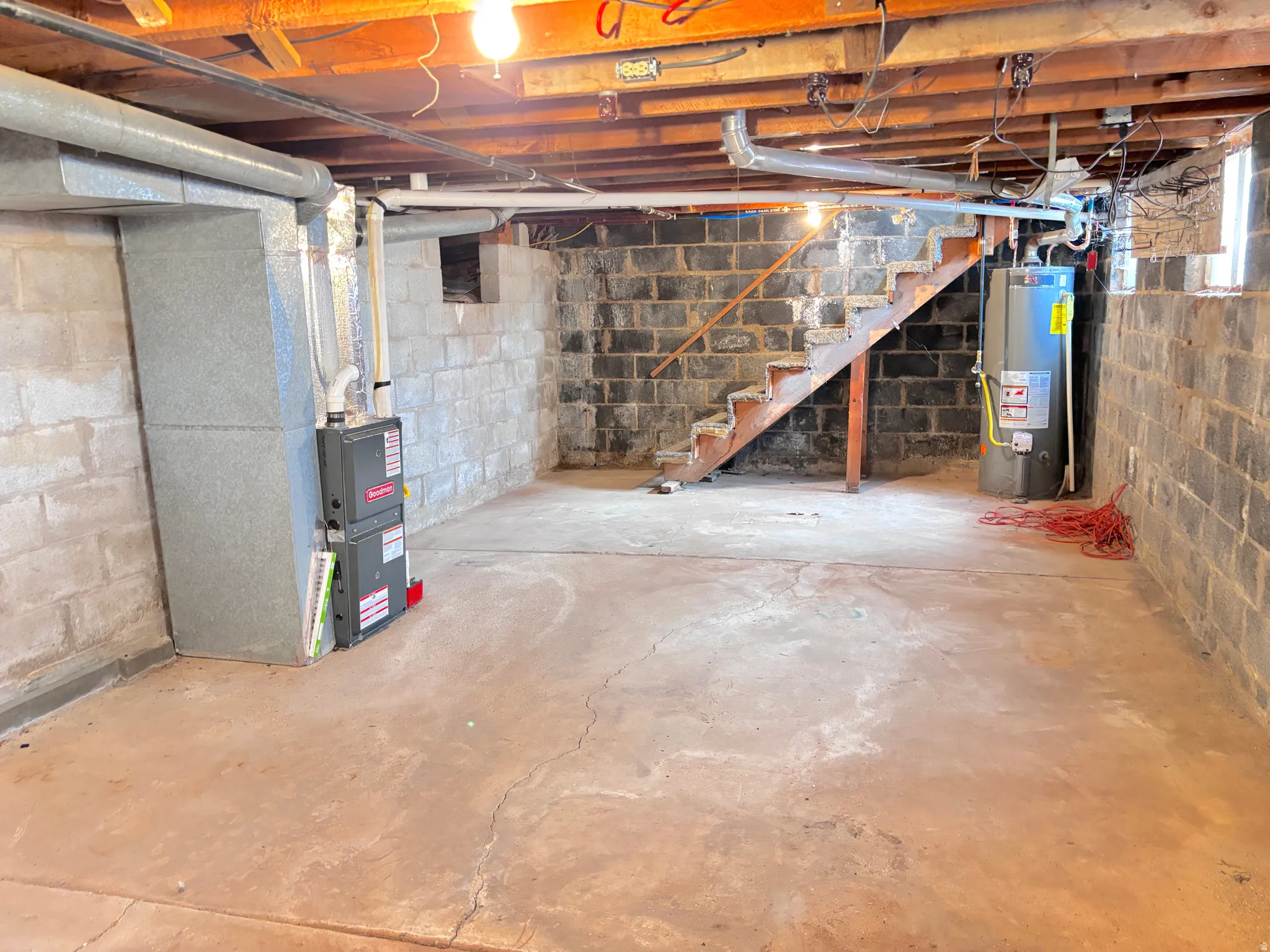 Unfinished basement with concrete flooring, exposed ceiling joists, and a visible water heater