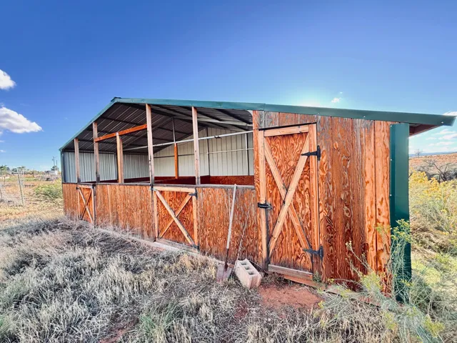 Wood-sided outbuilding with a green metal roof, multiple stalls, and an enclosed storage area