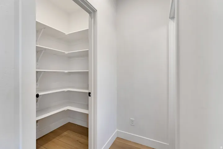 Walk-in pantry featuring white shelving and wood-finish flooring