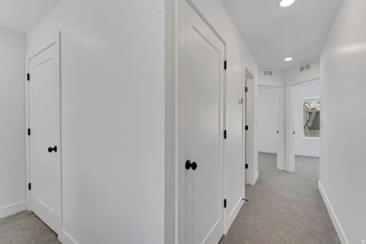 Hallway with neutral carpeting, white walls, recessed lighting, and white doors with matte black hardware