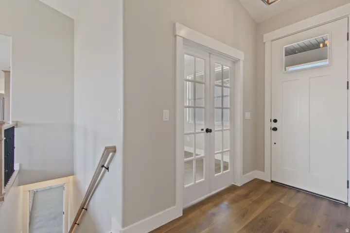 Entryway with wood-finish flooring, white paneled door with transom, and double French doors