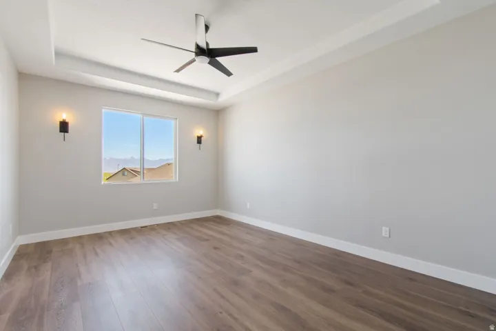 Recessed ceiling detail, wood-finish flooring, contemporary ceiling fan, dual wall sconces, and a large window