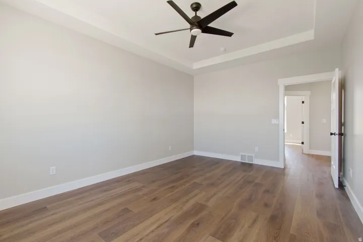 Tray ceiling with a ceiling fan, wood-finish flooring, white trim, and a white interior door with black hardware