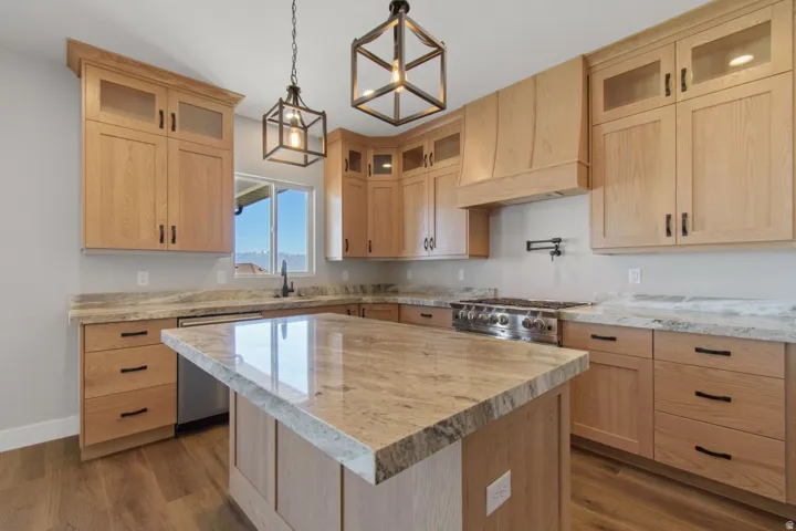 Kitchen featuring light wood-finish cabinetry, stone countertops, stainless steel appliances, a center island, and pendant lighting