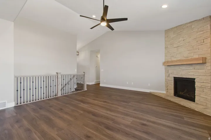 Vaulted ceiling, stone-clad fireplace with wood mantel, wood-finish flooring, ceiling fan, and recessed lighting