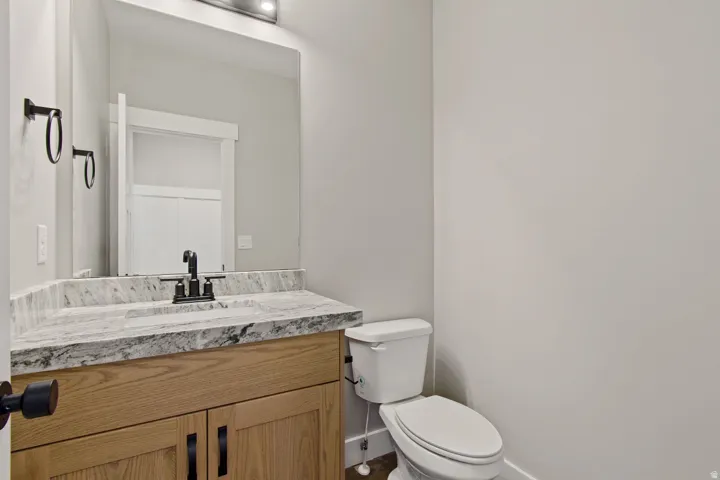 Light-toned wood vanity with dark hardware, undermount sink, granite countertop, and wall-mounted mirror with integrated lighting