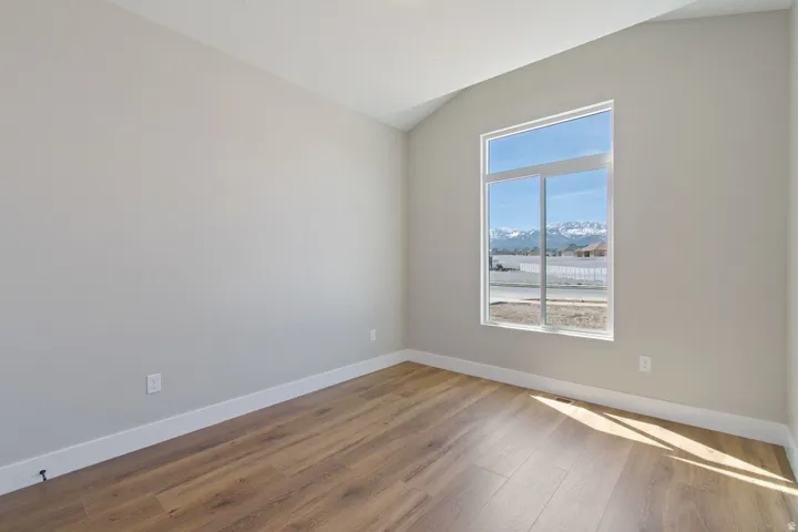 Sloped vaulted ceiling, light neutral wall paint, wood-finish flooring, white trim, and a large window with mountain scenery