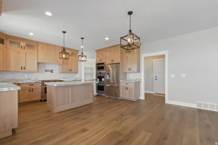 Kitchen featuring wood-finish flooring, light wood cabinetry, a central island, stainless steel appliances, and pendant lighting