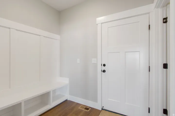Built-in bench with storage, wood-finish flooring, white paneled door, and neutral wall paint
