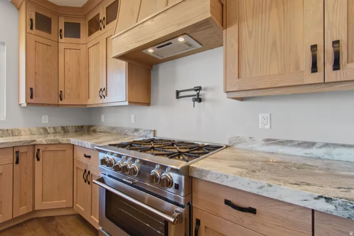 Wood-finish cabinetry with black hardware, stainless steel range with griddle, pot filler, coordinating range hood, and stone countertops
