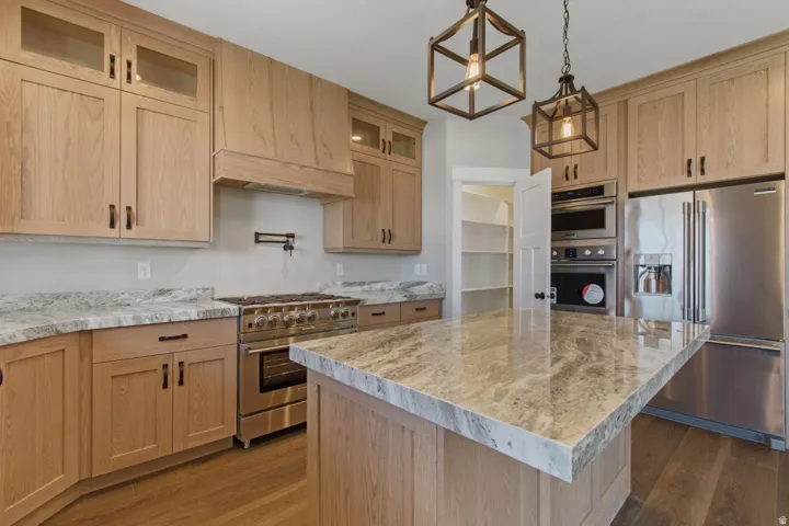 Wood-finish cabinetry with dark hardware, stone countertops, stainless steel appliances, and wood-finish flooring