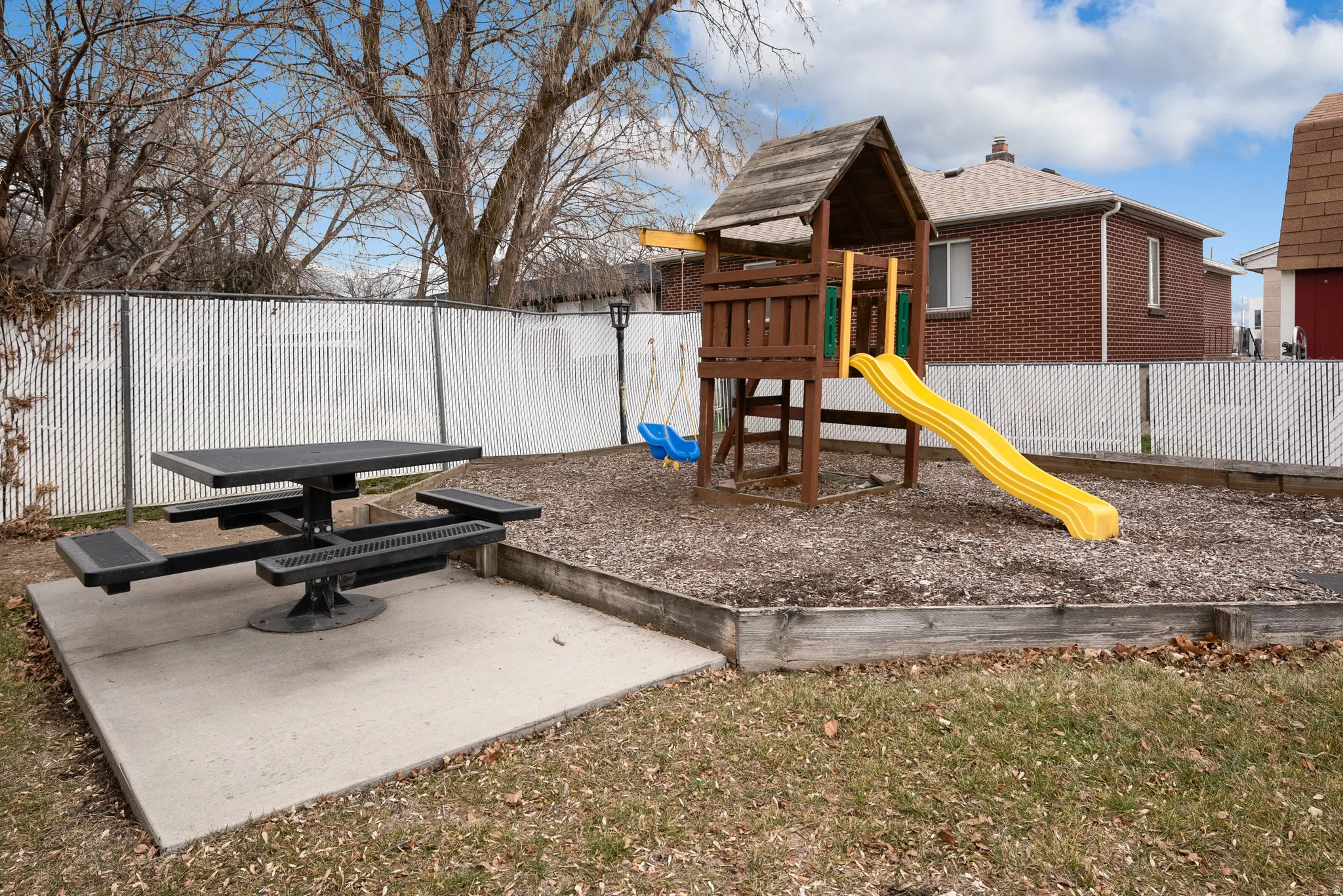 Outdoor entertainment area with a picnic table on a concrete pad, a raised play structure.