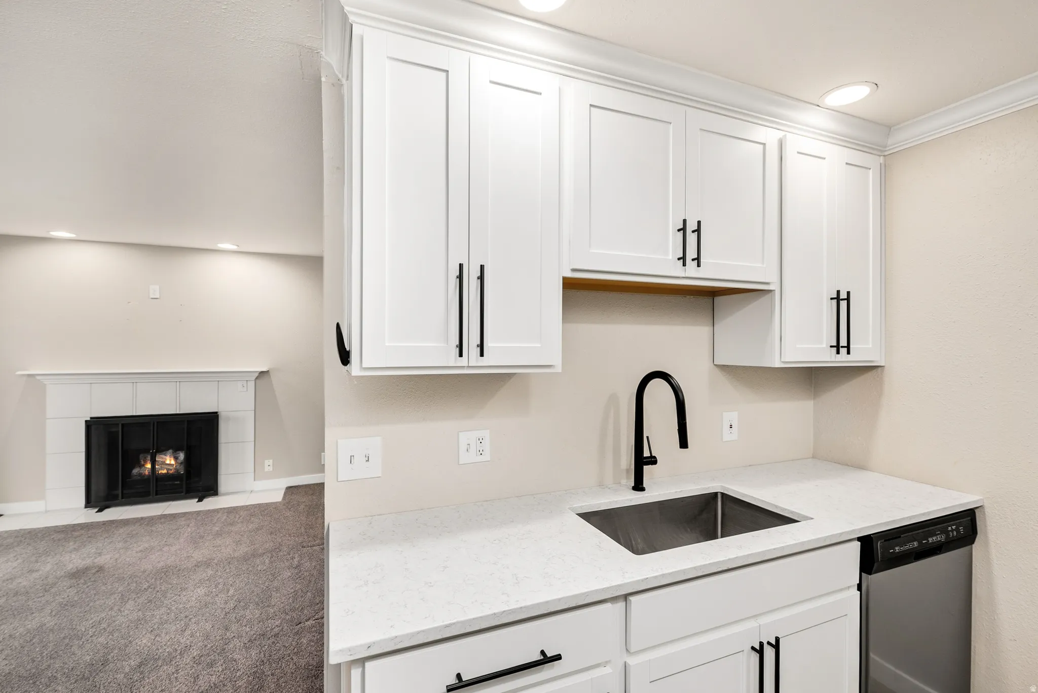White shaker-style cabinetry with matte black hardware, stainless steel undermount sink with gooseneck faucet, light-toned countertops, and built-in dishwasher