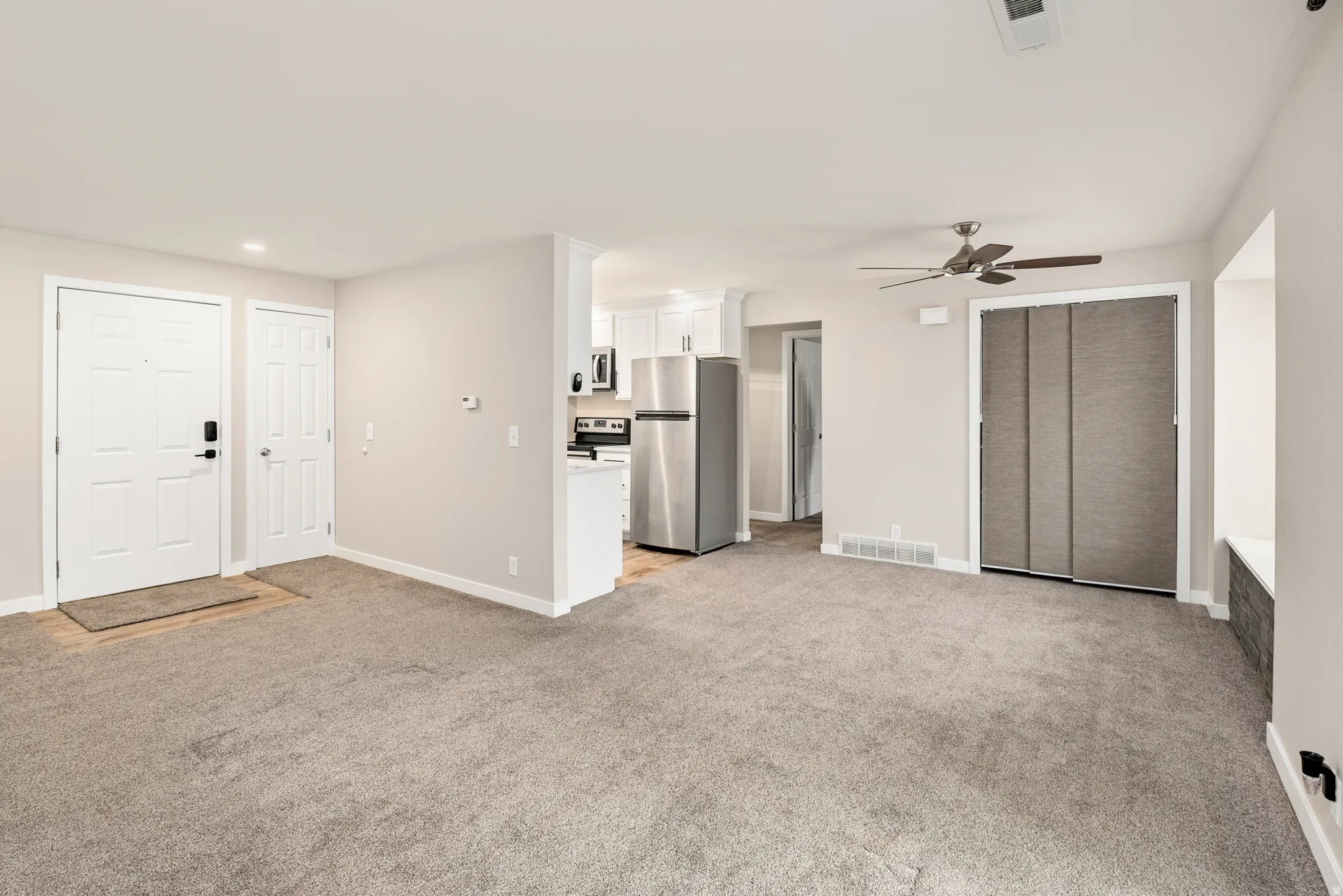 Expansive carpeted living area with a ceiling fan, window seat.