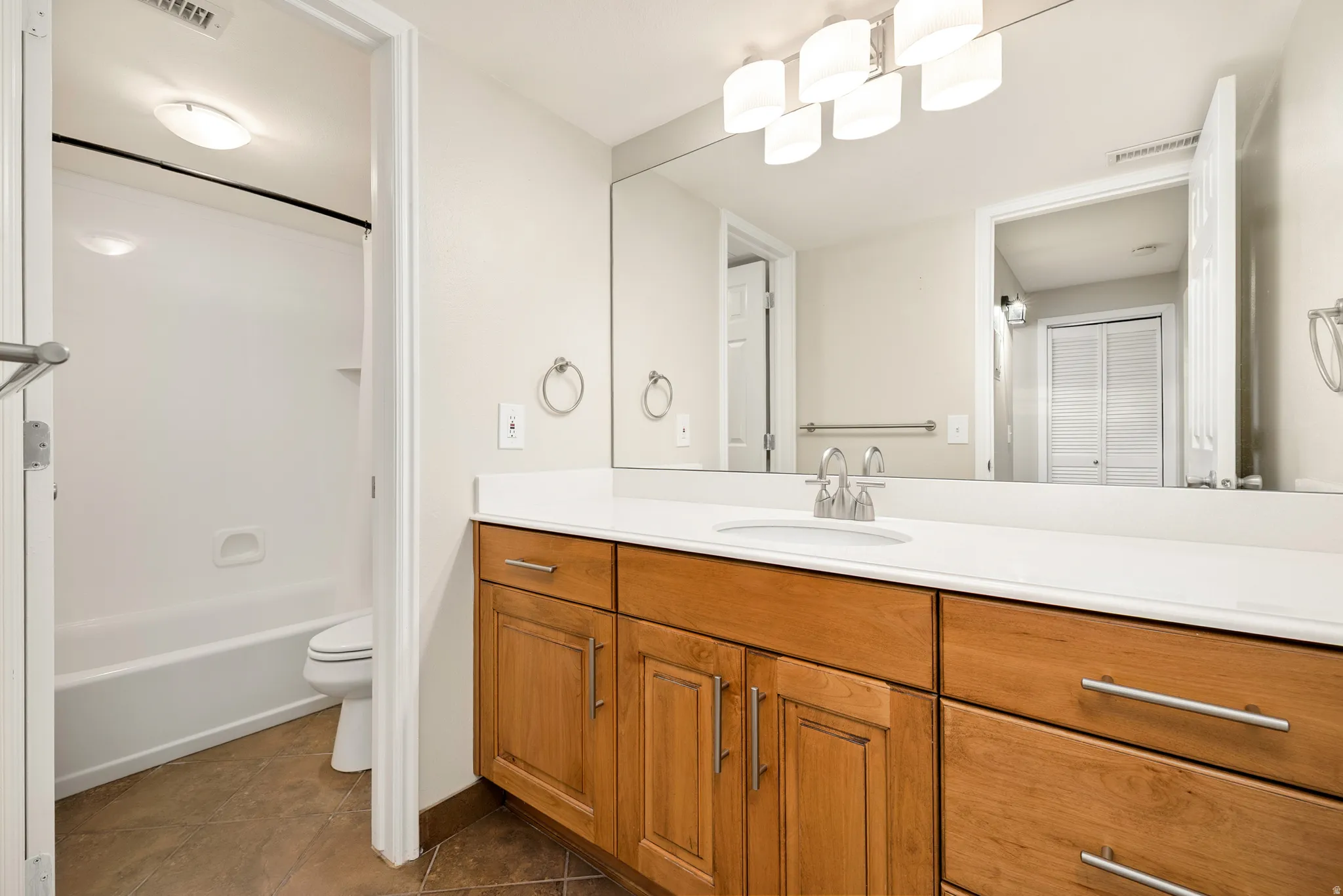 Bathroom featuring a wide wood-finish vanity with a light-toned countertop, a large wall-mounted mirror, a modern vanity light fixture, and a tub/shower combination