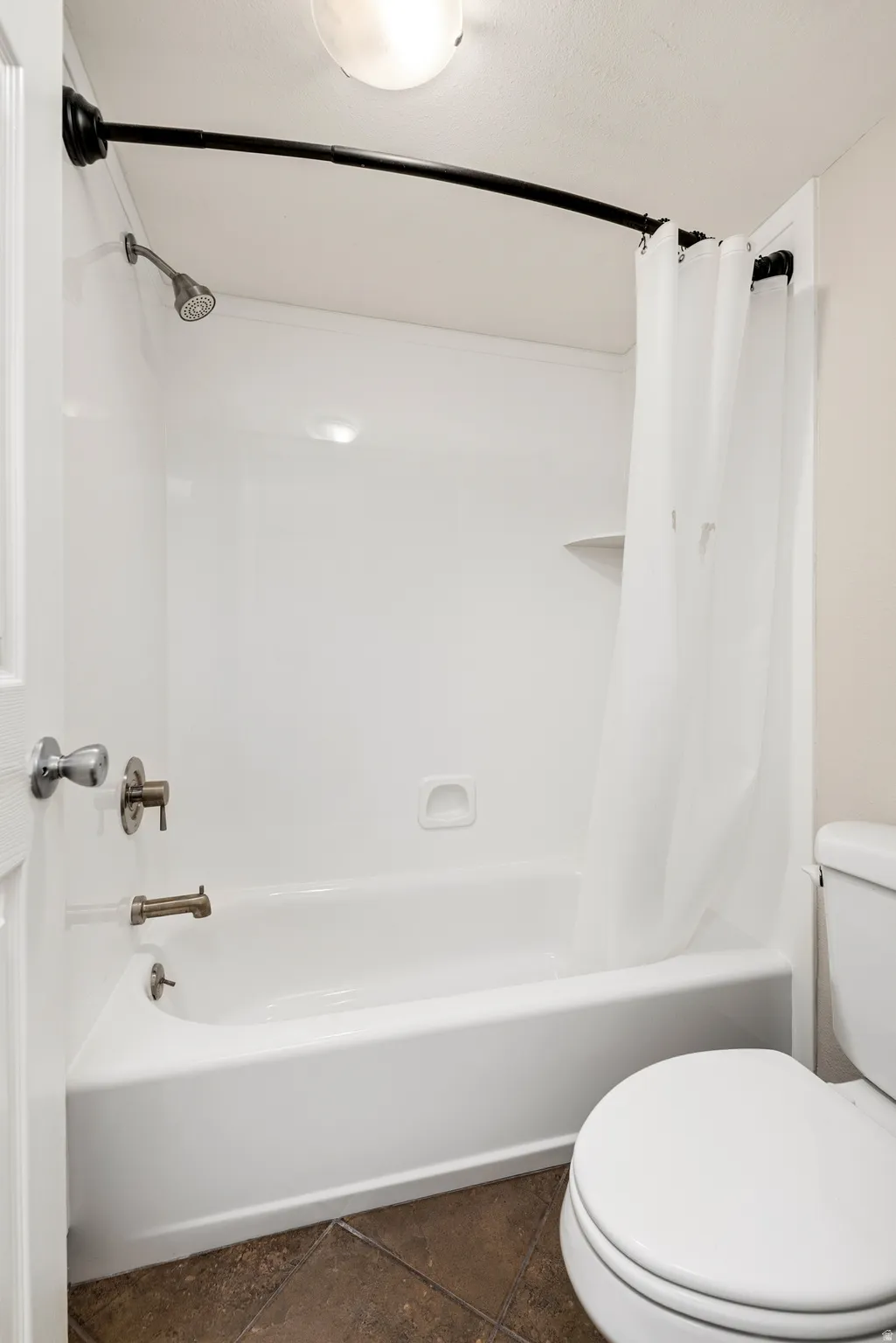 White bathtub and shower combination with brushed nickel fixtures, complemented by earth-toned tile flooring