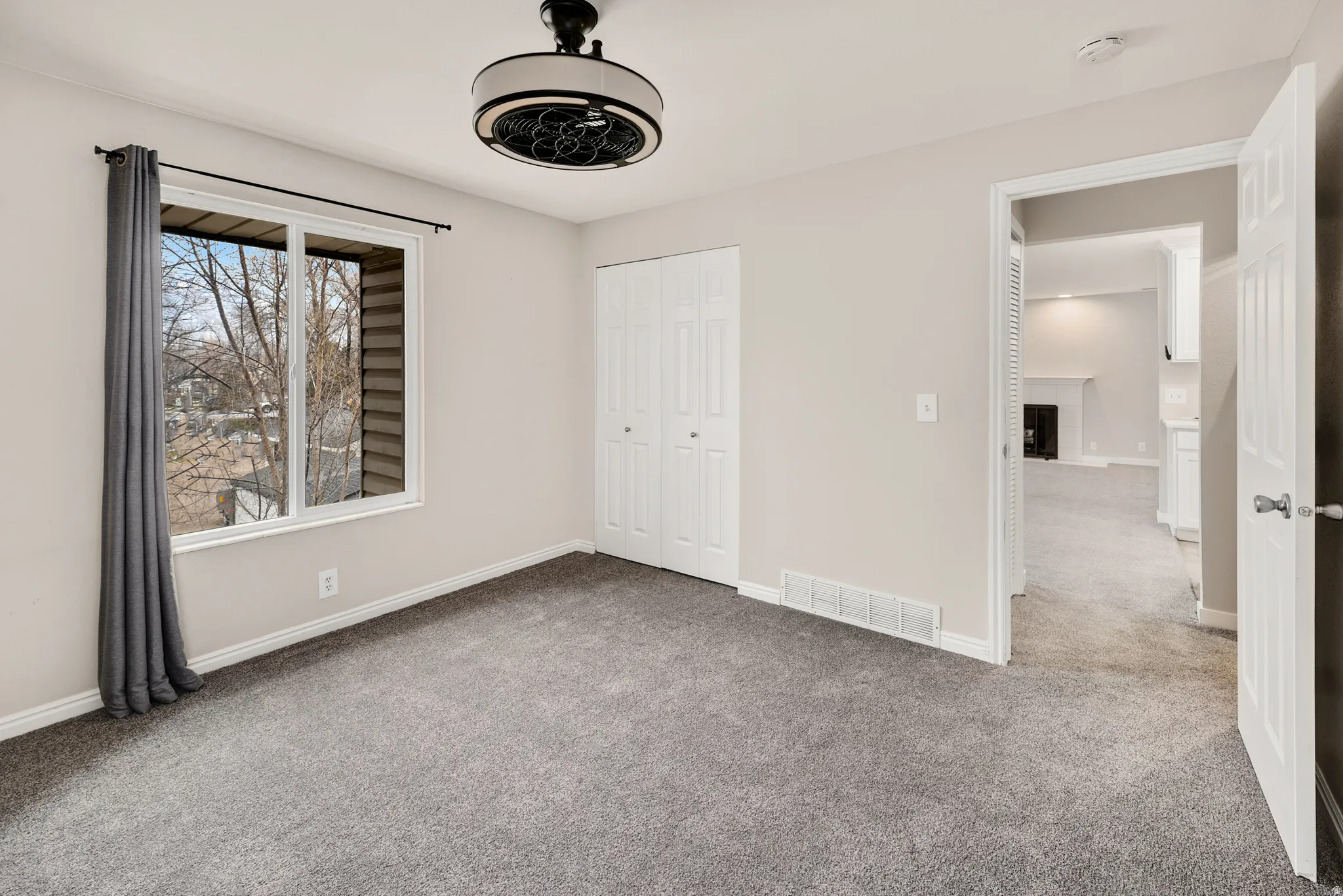 Light gray wall paint, gray carpeting, white trim, and a ceiling-mounted light fixture with fan