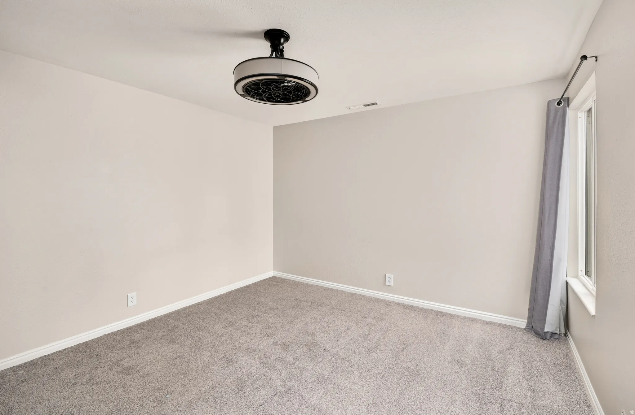 Neutral wall paint, light gray carpeting, ceiling-mounted light fixture, window with trim, and white baseboards