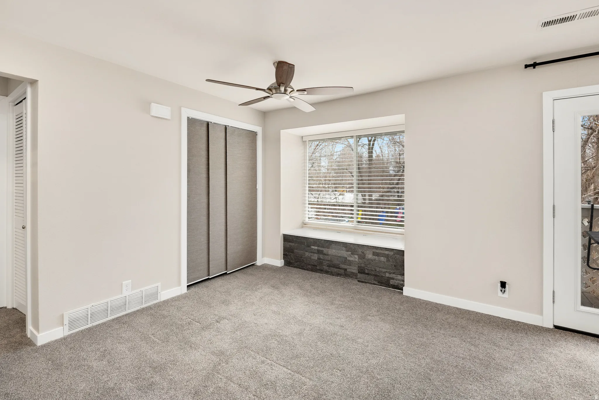 Recessed window with stone-finish base, ceiling fan, and grey carpet