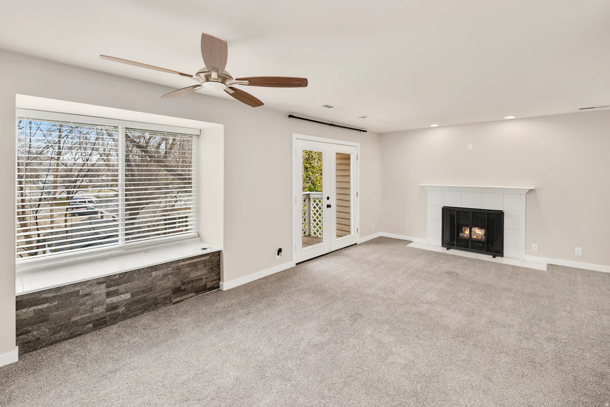 Recessed lighting, ceiling fan, carpet flooring, and a fireplace with a white tile surround