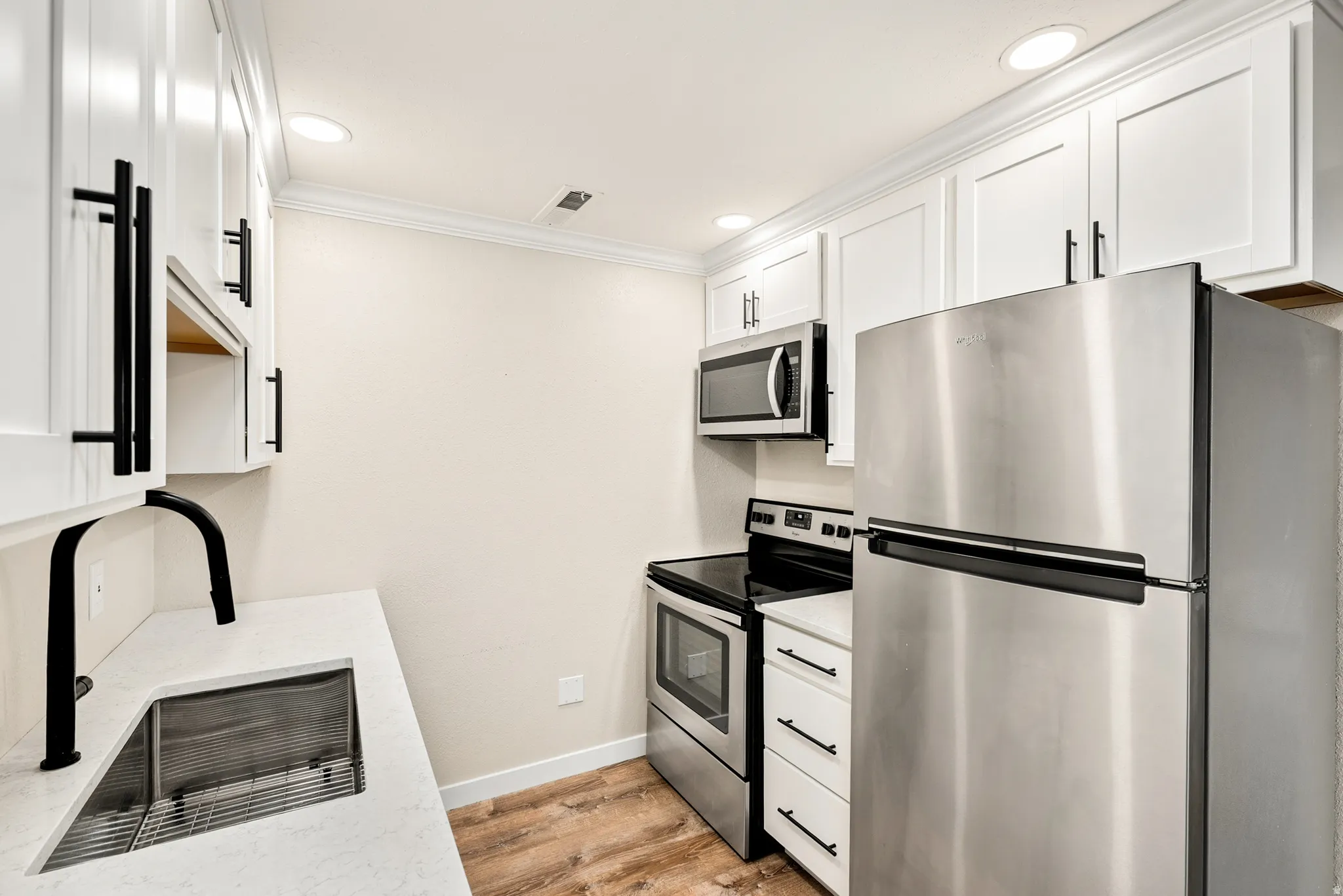 White shaker cabinetry with matte black hardware, stainless steel appliances, wood-finish flooring, and recessed ceiling lighting