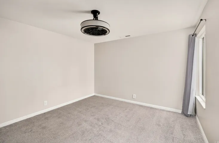 Neutral wall paint, light gray carpeting, ceiling-mounted light fixture, window with trim, and white baseboards