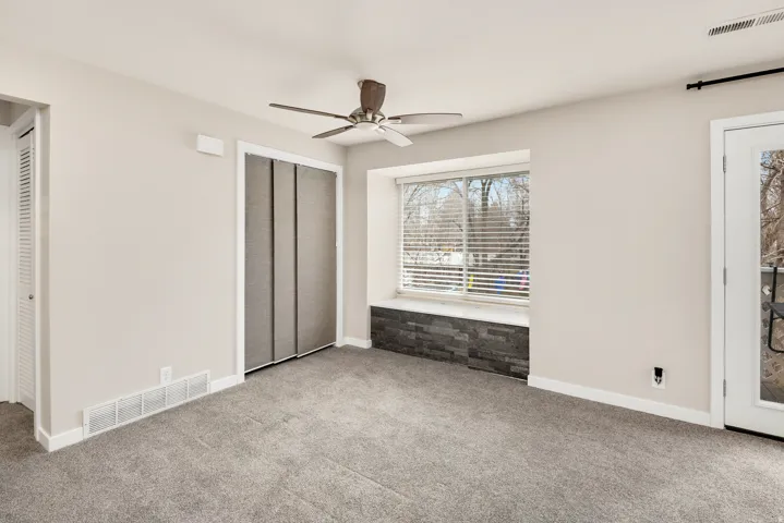Recessed window with stone-finish base, ceiling fan, and grey carpet