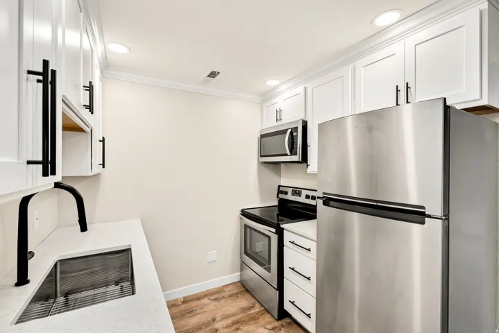 White shaker cabinetry with matte black hardware, stainless steel appliances, wood-finish flooring, and recessed ceiling lighting