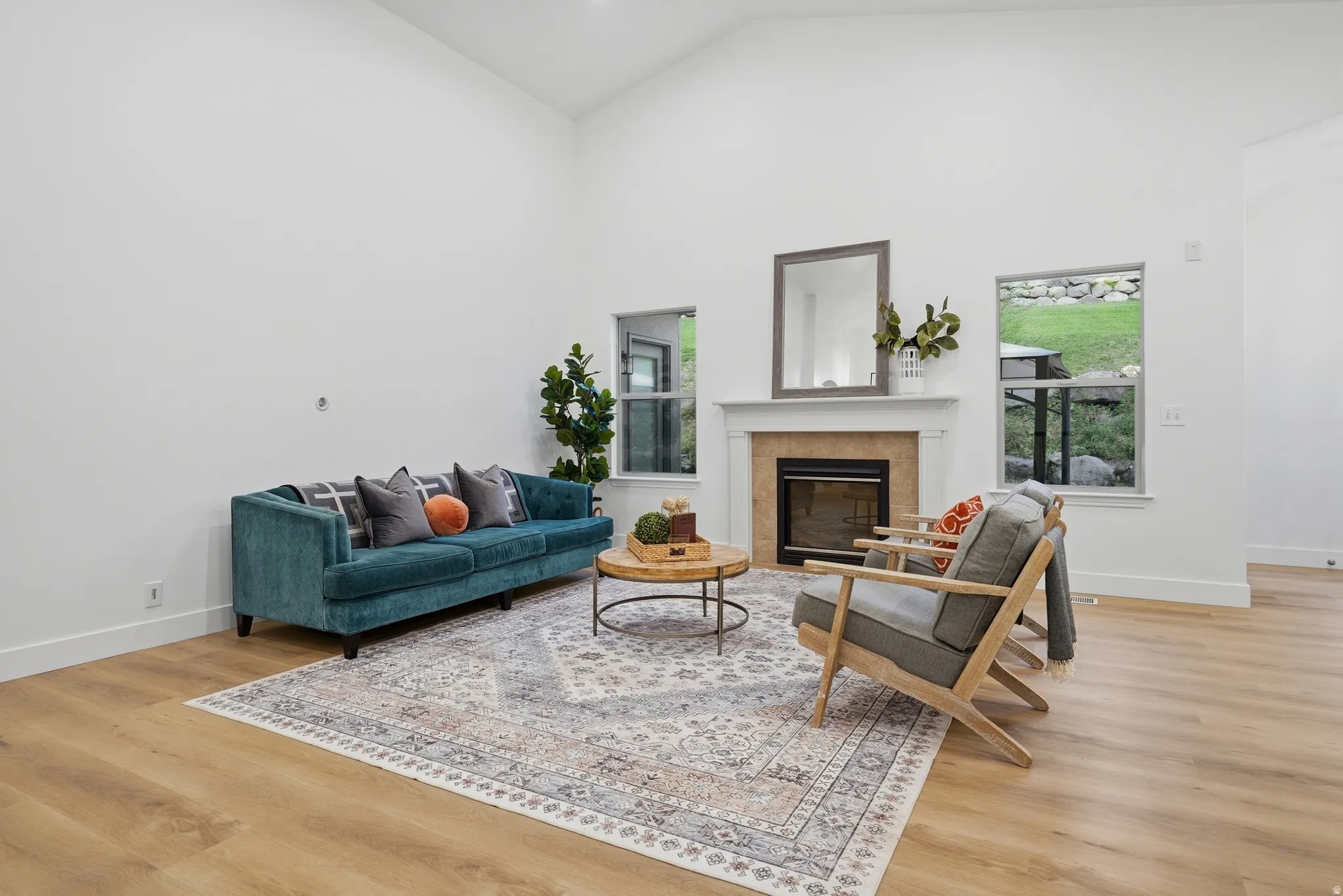 Living room with vaulted ceilings, wood-finish LVP flooring, fireplace with stone surround, and multiple windows