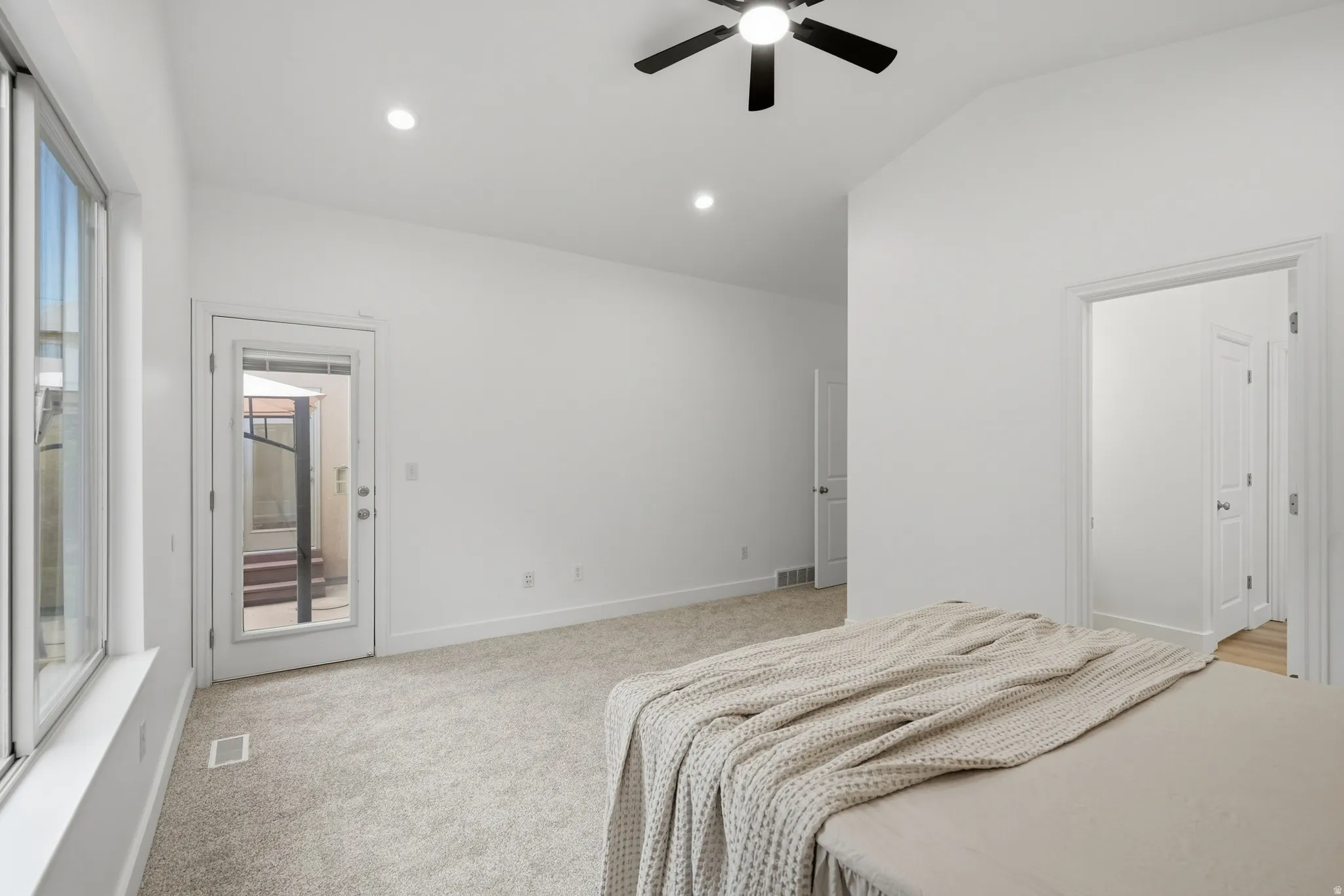 Primary bedroom with vaulted ceiling, recessed lighting, ceiling fan, carpet flooring, and a glass-paneled door leading to backyard patio