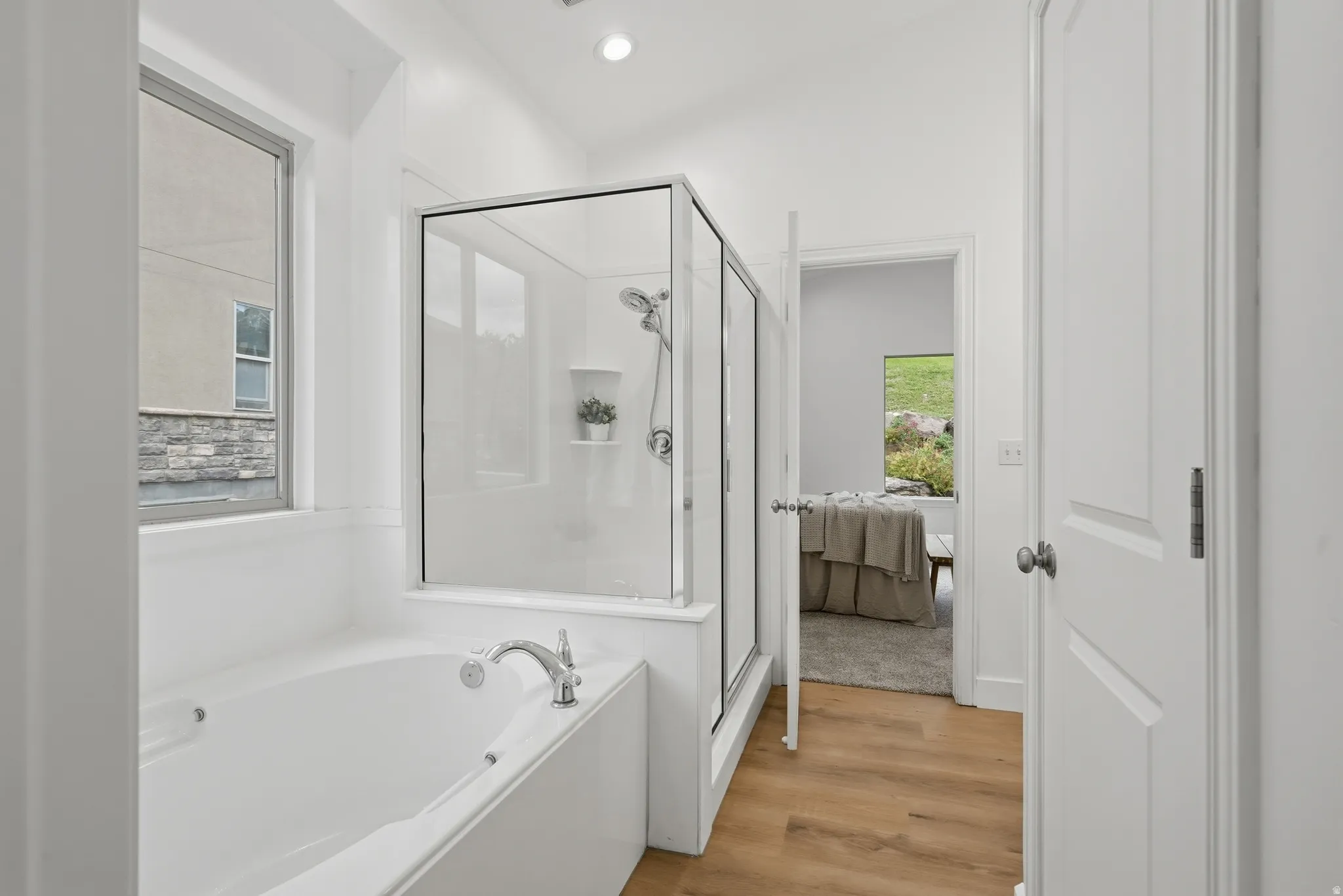 Primary bath with soaking tub with chrome fixtures, glass-enclosed shower, wood-finish LVP flooring, and recessed lighting