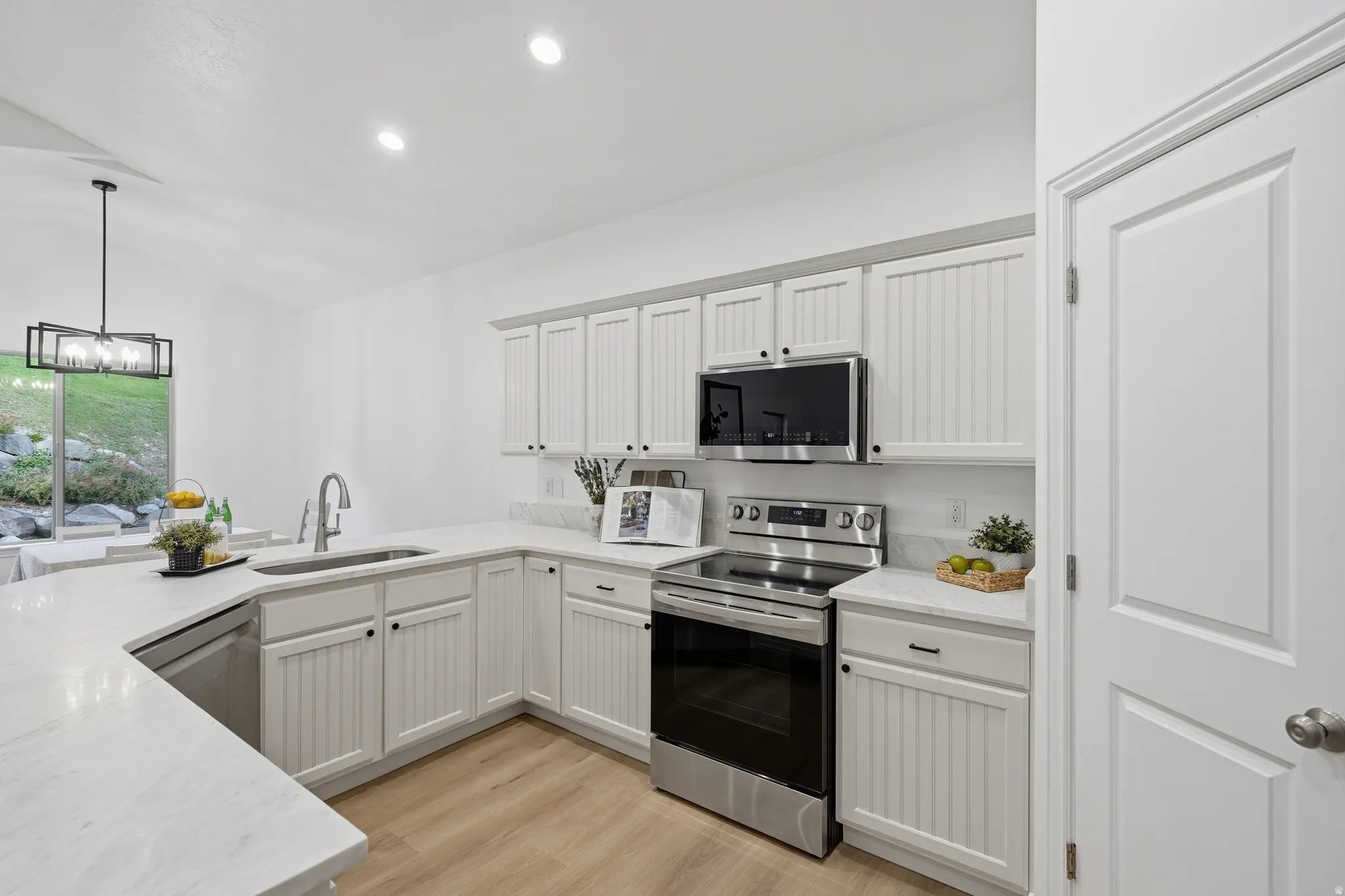 Kitchen featuring light cabinetry with beadboard paneling, stainless steel appliances, golden taj quartz countertops, wood-finish LVP flooring, and recessed lighting