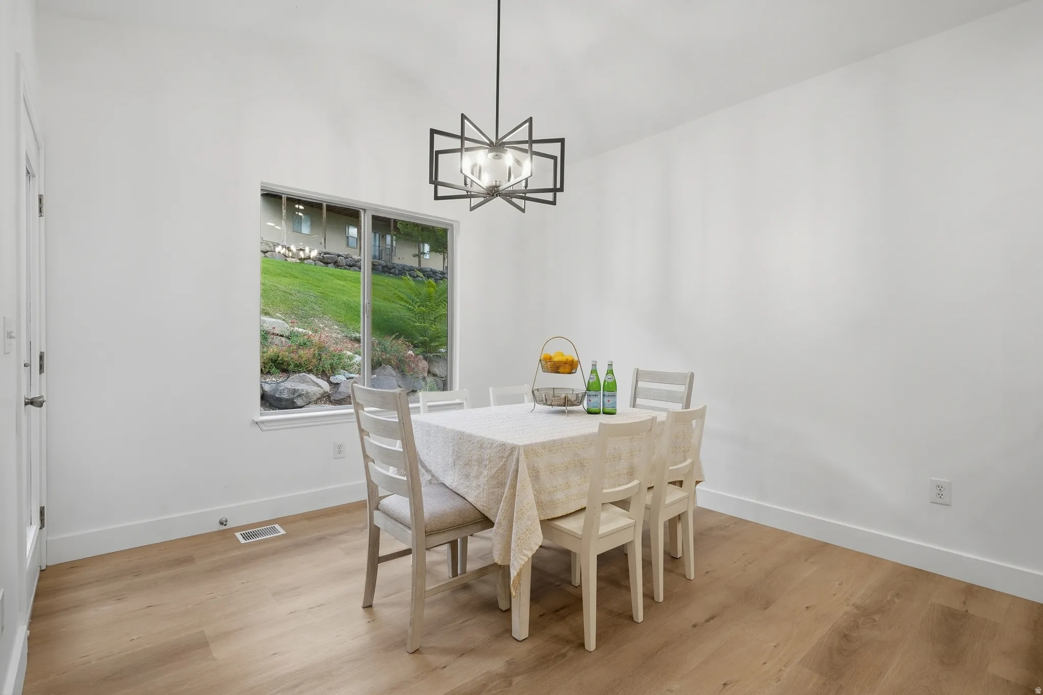Dining area with wood-finish LVP flooring, white walls, contemporary ceiling light fixture, and access to backyard patio