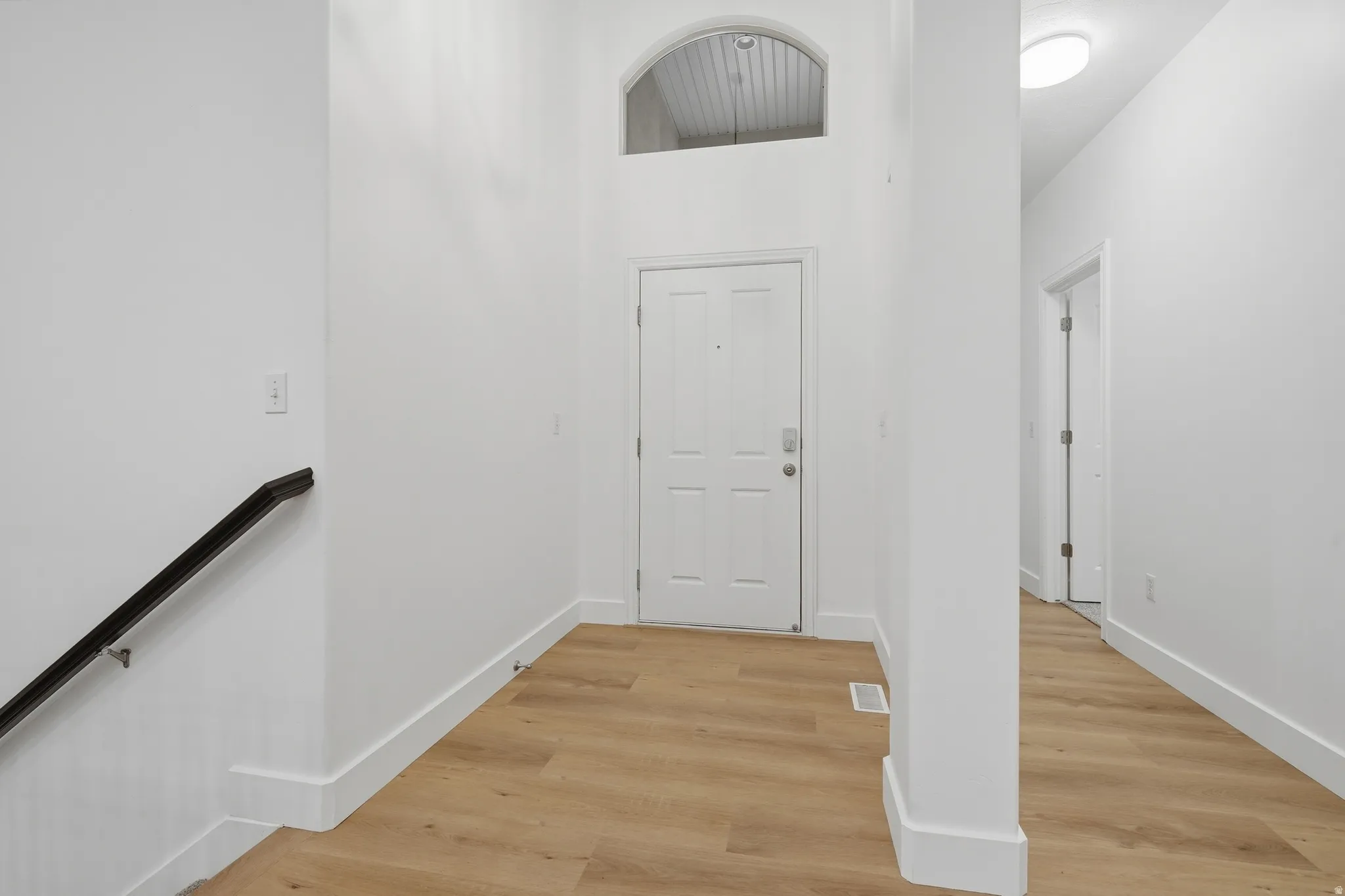 Entryway with wood-finish LVP flooring, white paneled door, and arched transom window