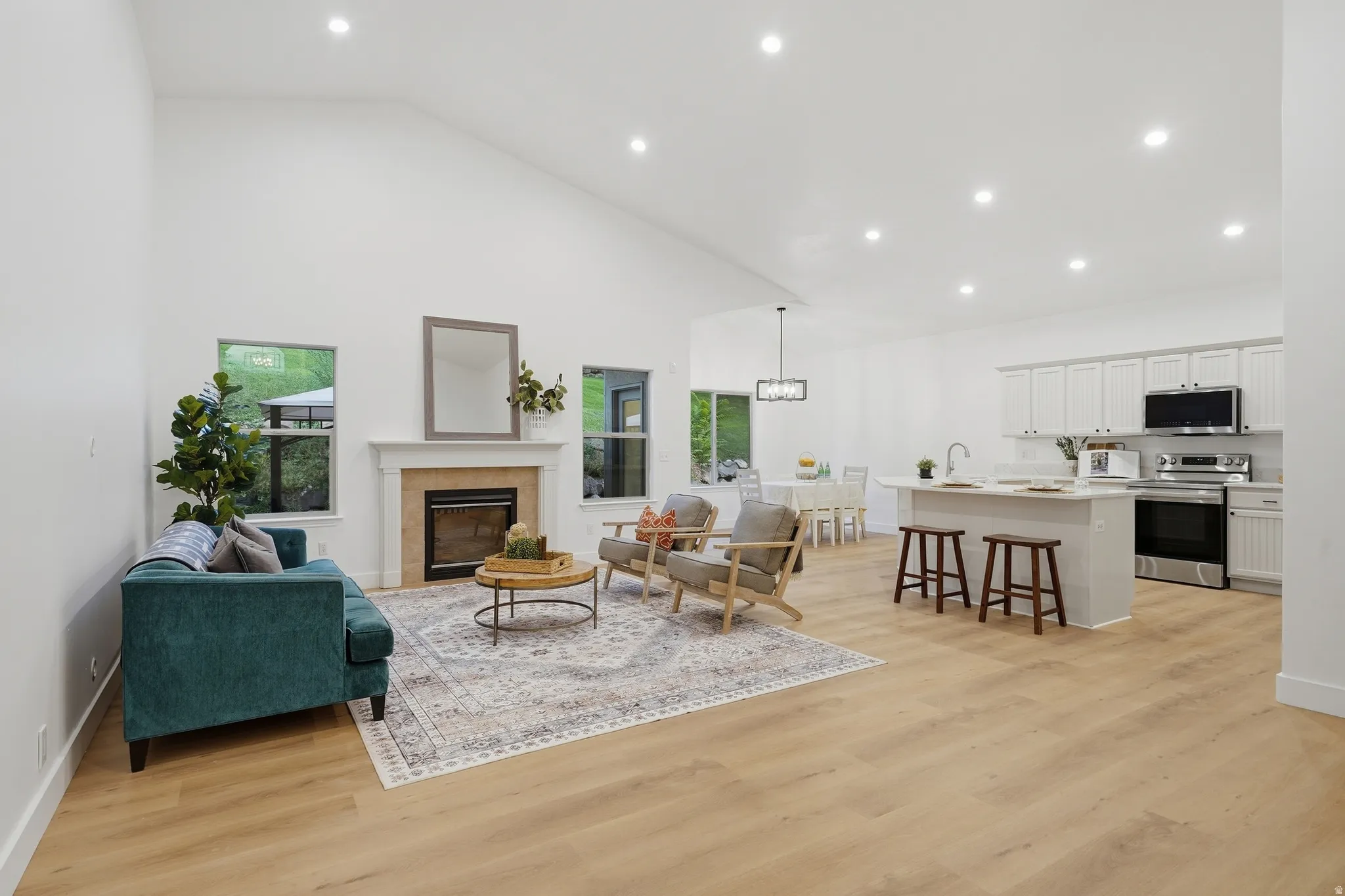 Open concept living room with vaulted ceilings, a built-in fireplace with a stone surround, wood-finish LVP flooring, a kitchen island with seating, and white cabinetry