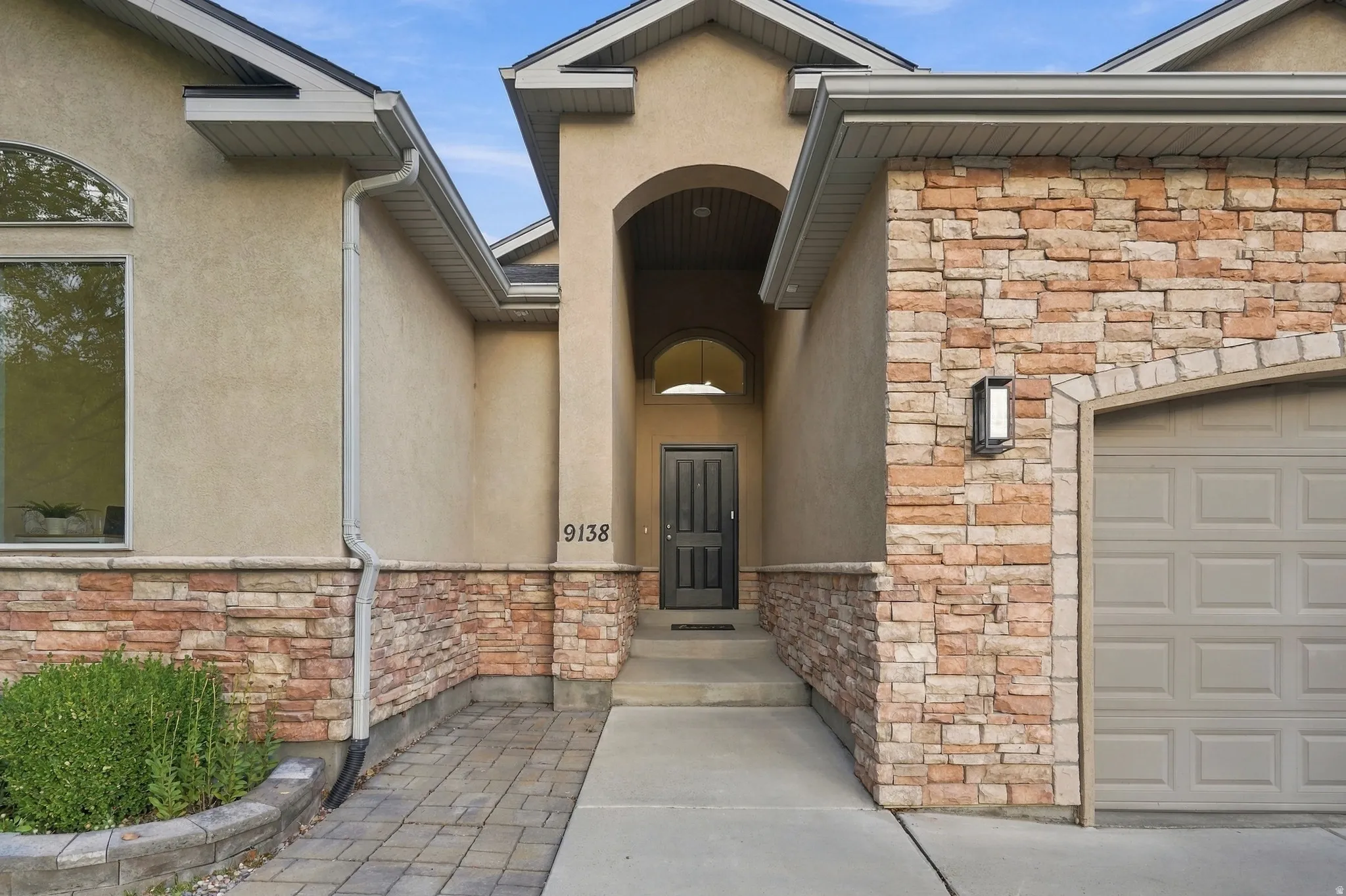 Stucco and stone home with an arched entry and covered porch