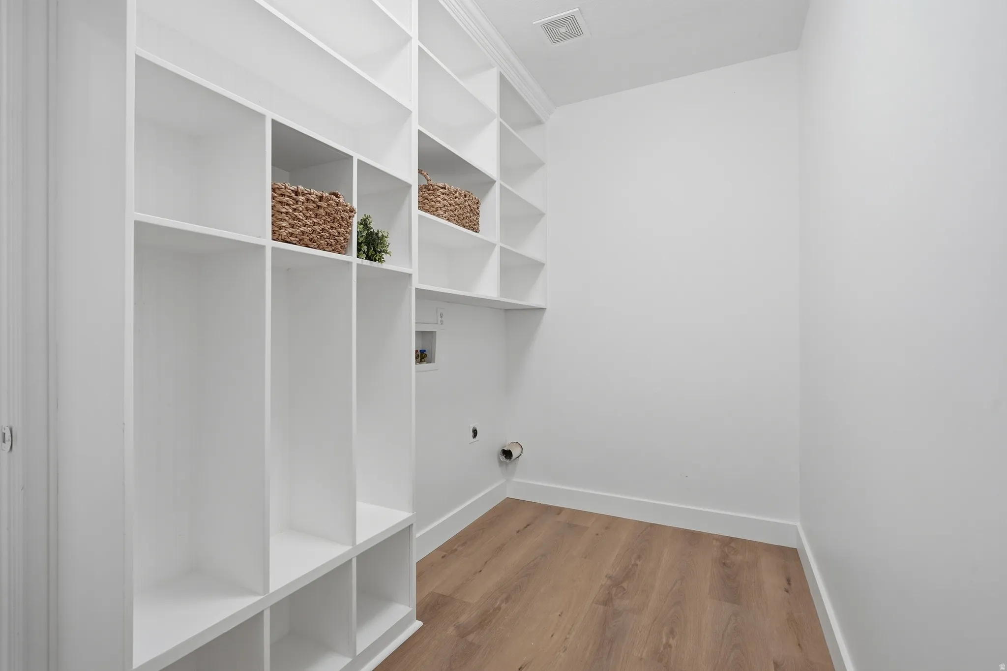 Laundry/mudroom with built-in shelving, wood-finish LVP flooring, white walls, and dedicated laundry hookups. Access to the garage.