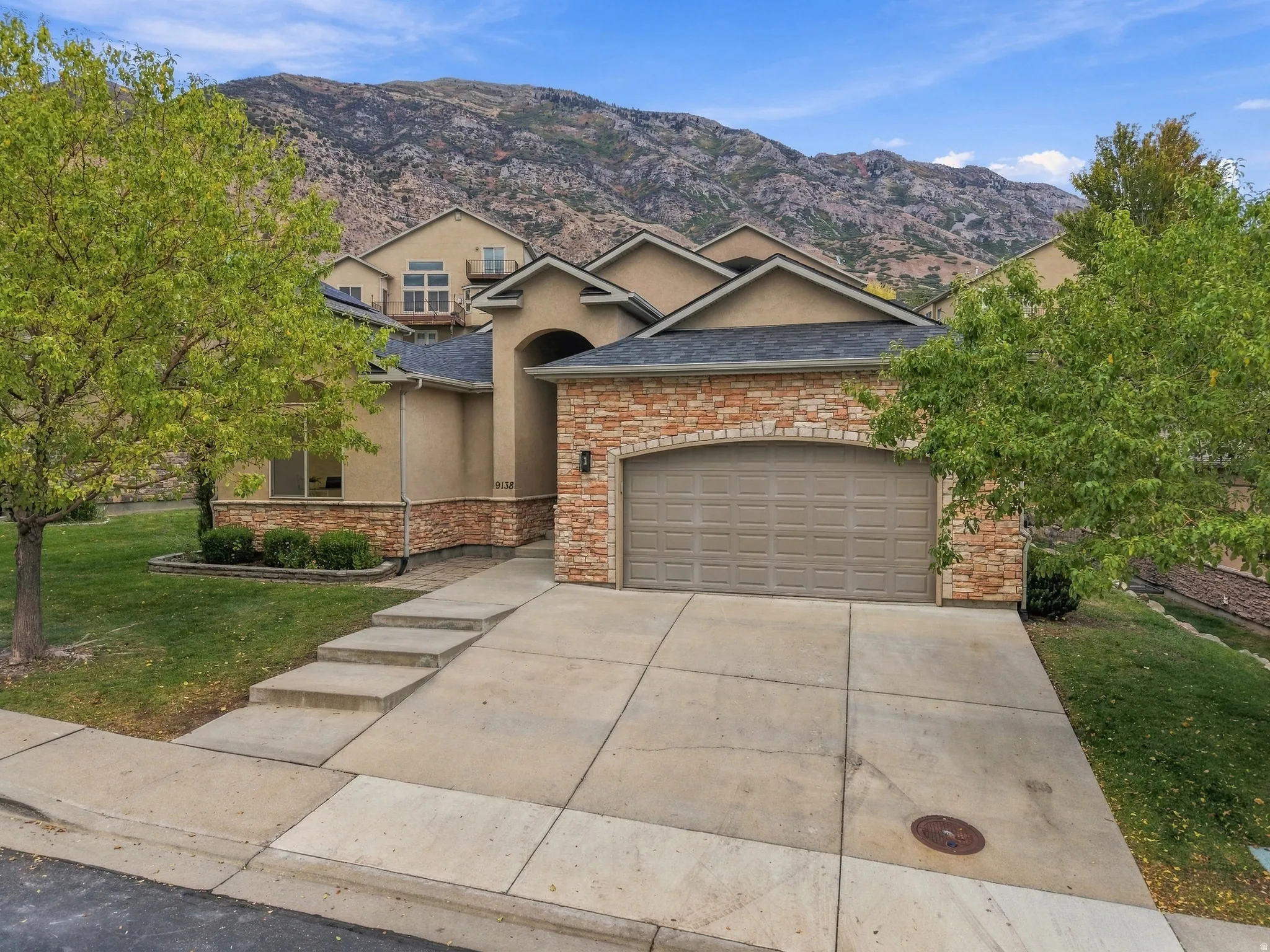 Stucco exterior with stone accenting, arched entry, two-car garage, concrete driveway, and mature landscaping