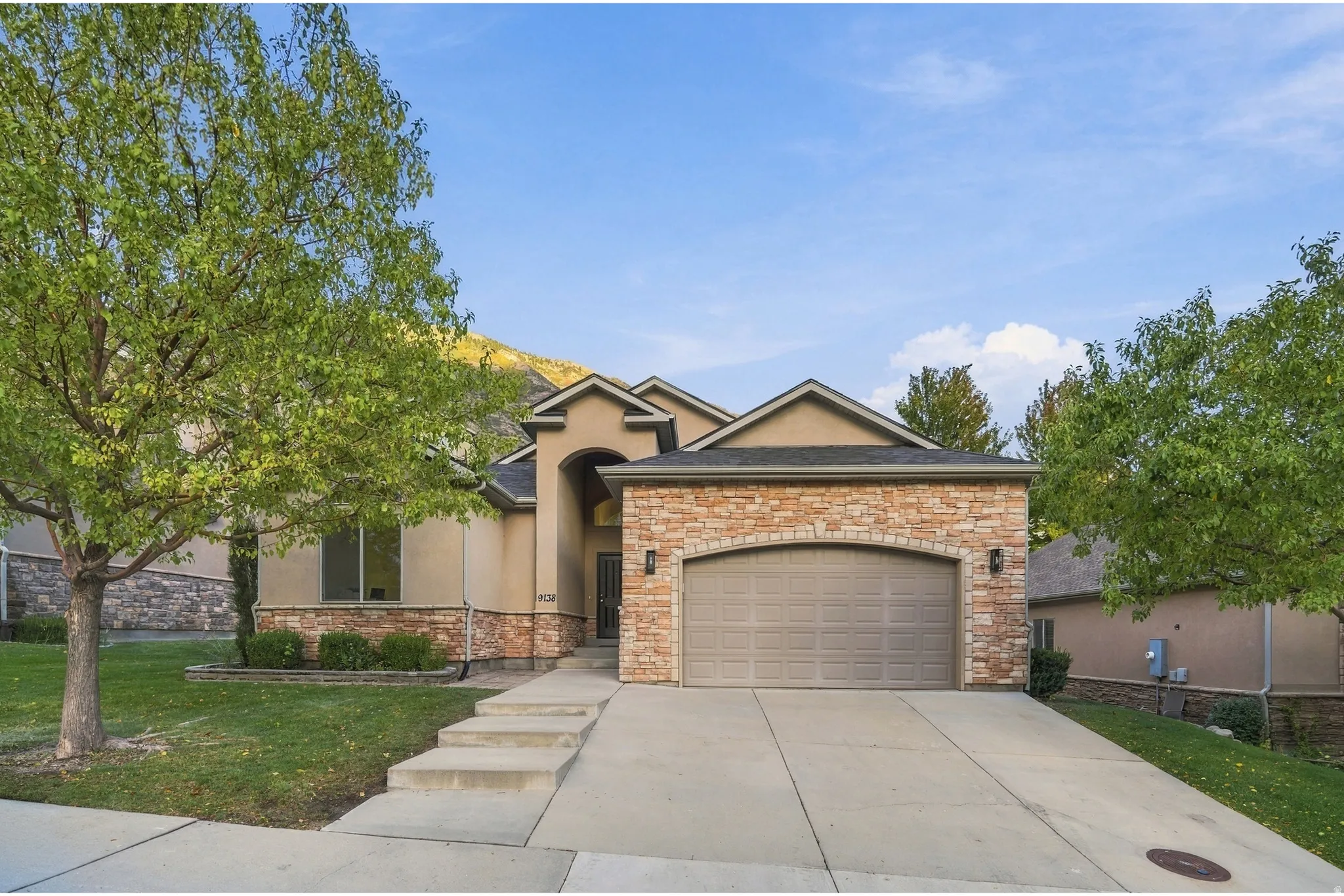 Stucco exterior with stone accents, a two-car garage, and a concrete driveway