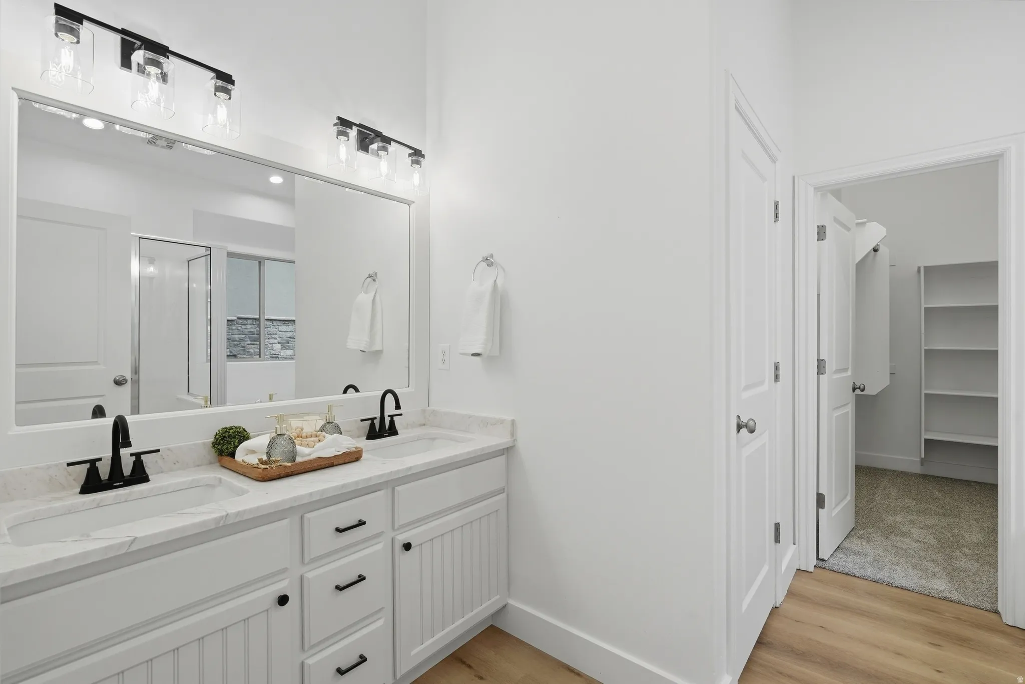 Primary bath with dual vanity with quartz countertop, matte black fixtures, toilet room and walk in closet