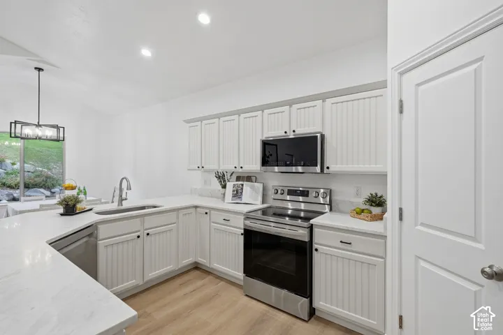 Kitchen featuring light cabinetry with beadboard paneling, stainless steel appliances, golden taj quartz countertops, wood-finish LVP flooring, and recessed lighting