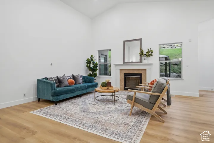 Living room with vaulted ceilings, wood-finish LVP flooring, fireplace with stone surround, and multiple windows