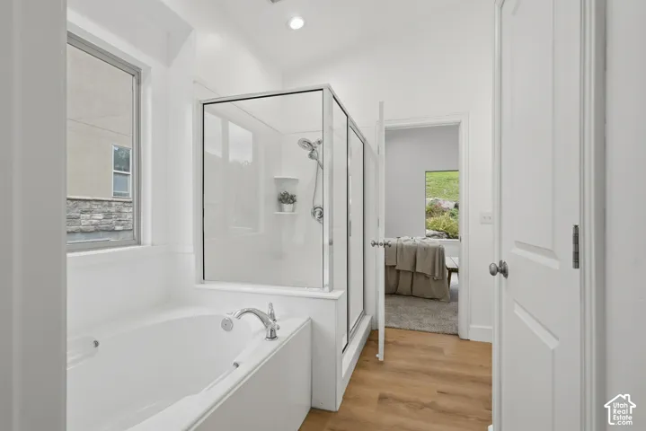 Primary bath with soaking tub with chrome fixtures, glass-enclosed shower, wood-finish LVP flooring, and recessed lighting