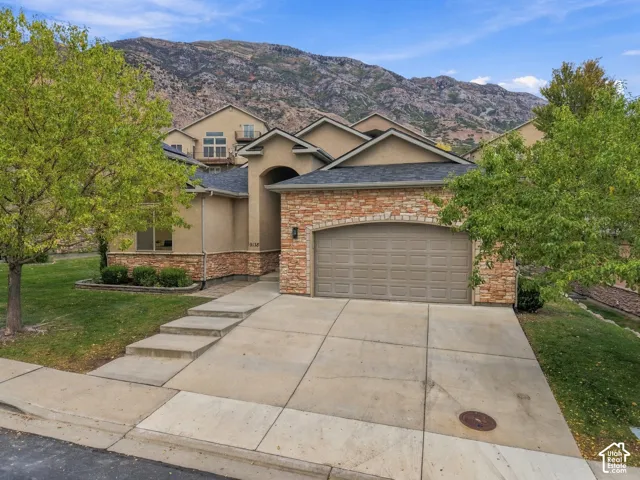 Stucco exterior with stone accenting, arched entry, two-car garage, concrete driveway, and mature landscaping