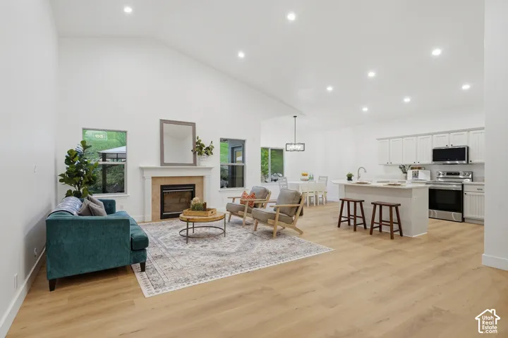 Open concept living room with vaulted ceilings, a built-in fireplace with a stone surround, wood-finish LVP flooring, a kitchen island with seating, and white cabinetry