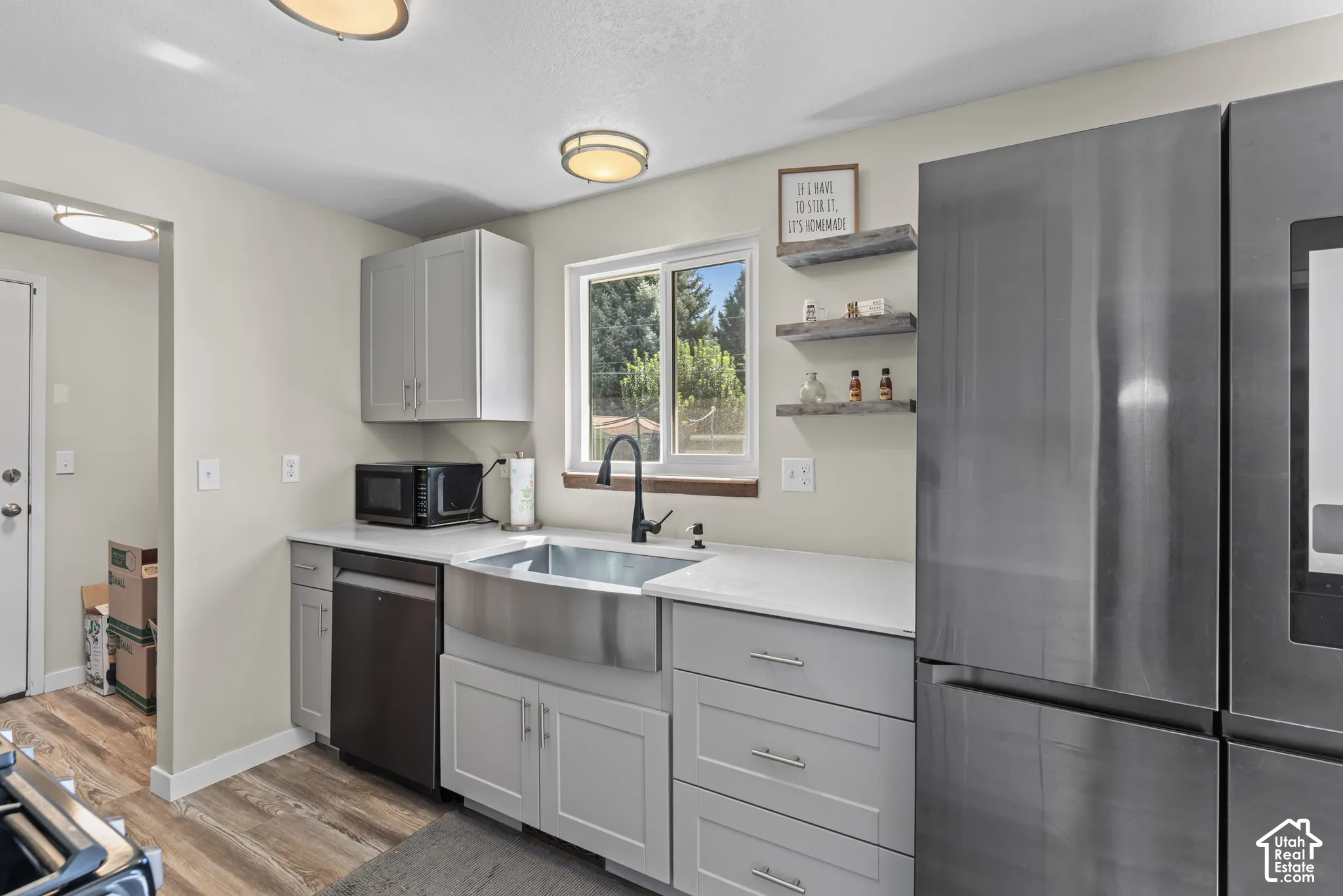 Modern kitchen with wood-finish flooring, light gray cabinetry, stainless steel farmhouse sink, and a black faucet