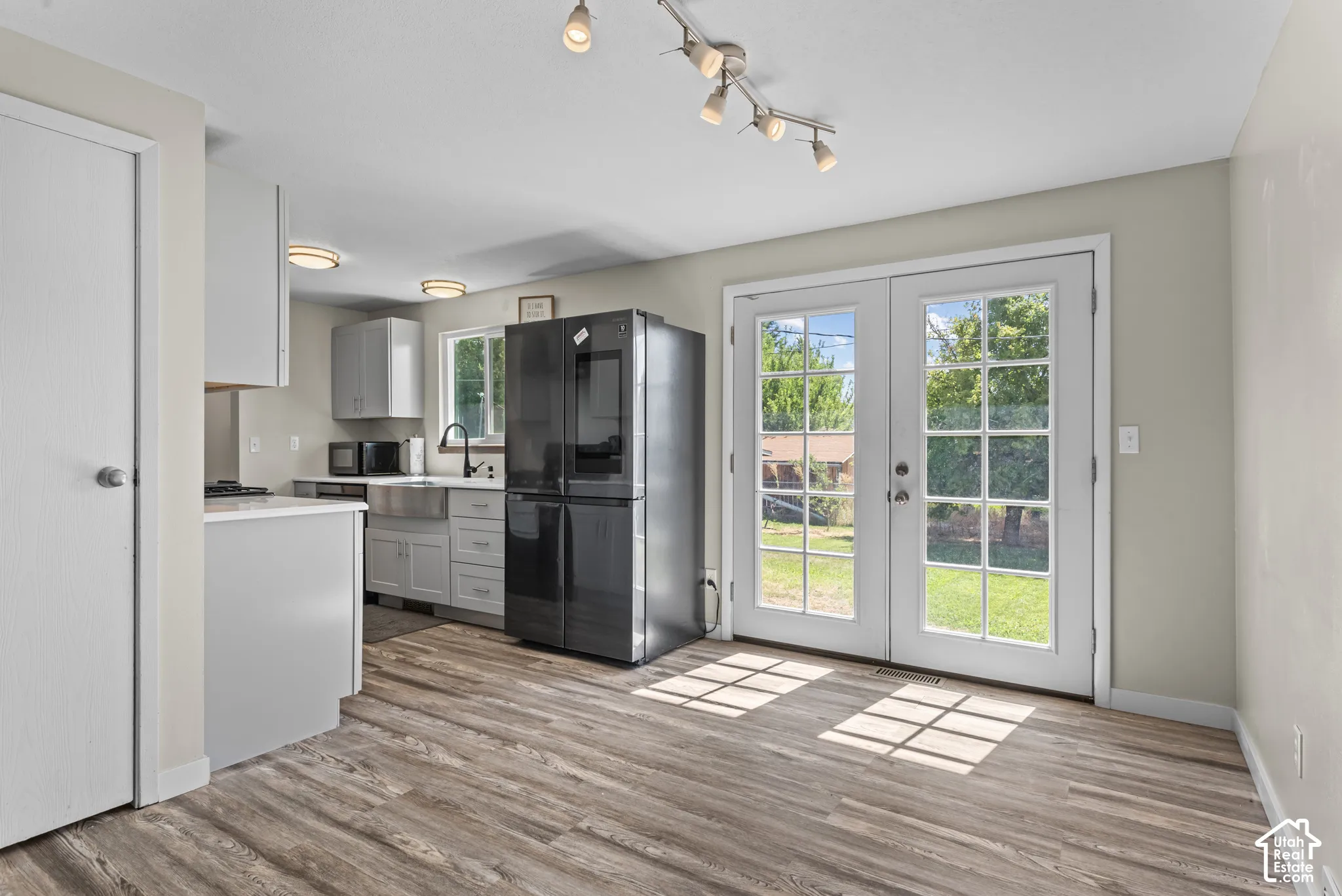 Wood-finish flooring throughout, with a kitchen featuring light cabinetry, a stainless steel farmhouse sink, and a black appliance package