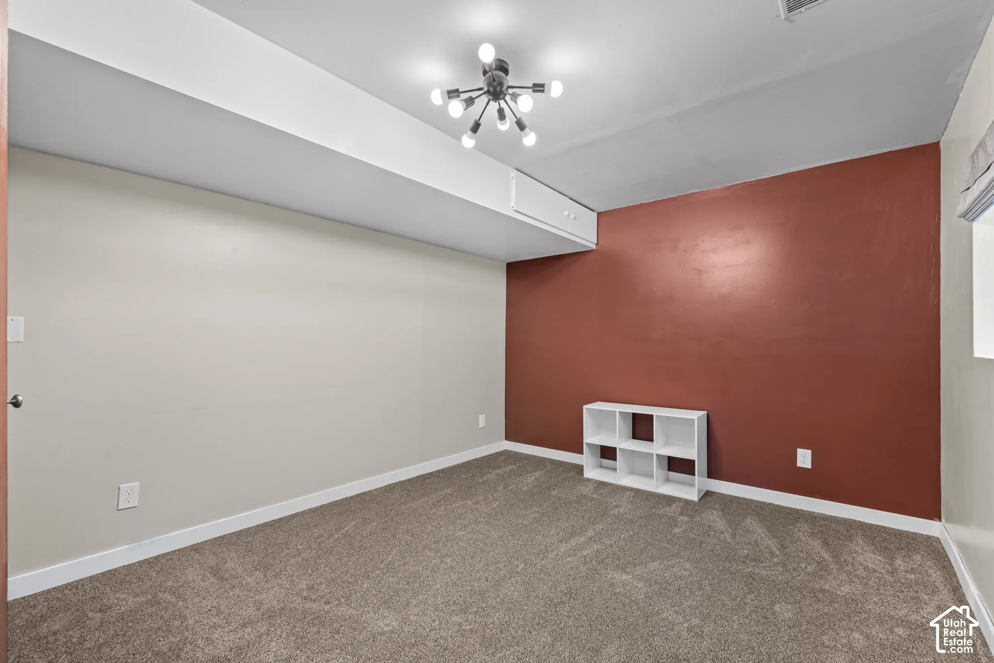 Plush carpet flooring, a modern sputnik chandelier, and a contrasting accent wall with white trim